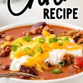 close up shot of a bowl of Chili Recipe topped with sour cream, shredded cheese, and diced green onions
