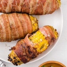 overhead shot of bacon-wrapped corn on the cob on a white plate