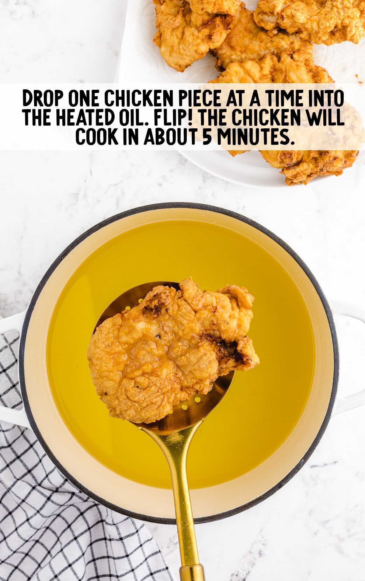 Golden fried chicken being lifted from hot oil in a pot, with instruction text saying it will cook in about 5 minutes