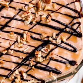 close up overhead shot of Turtle Poke Cake drizzled with caramel and chocolate sauce then sprinkled with pecans in a baking dish