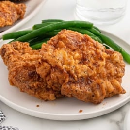 Plate of two fried pork chops with green beans on the side, ready to serve.